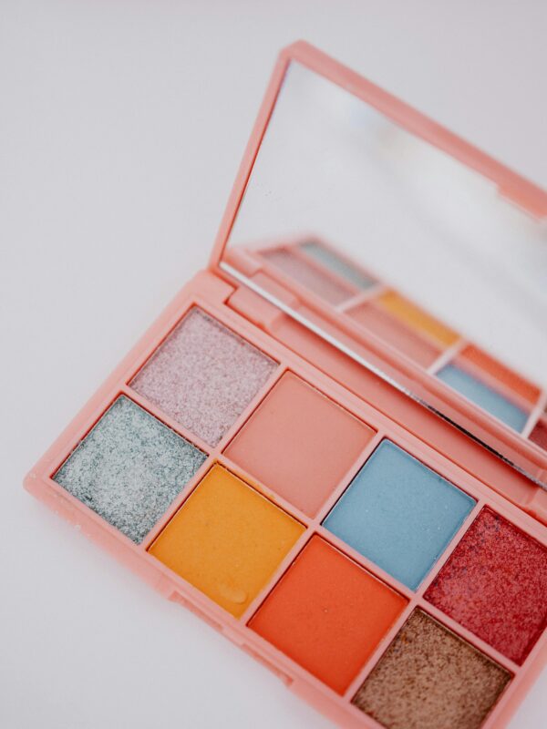 Colorful eyeshadow palette with mirror, featuring diverse shades, on a clean white background.