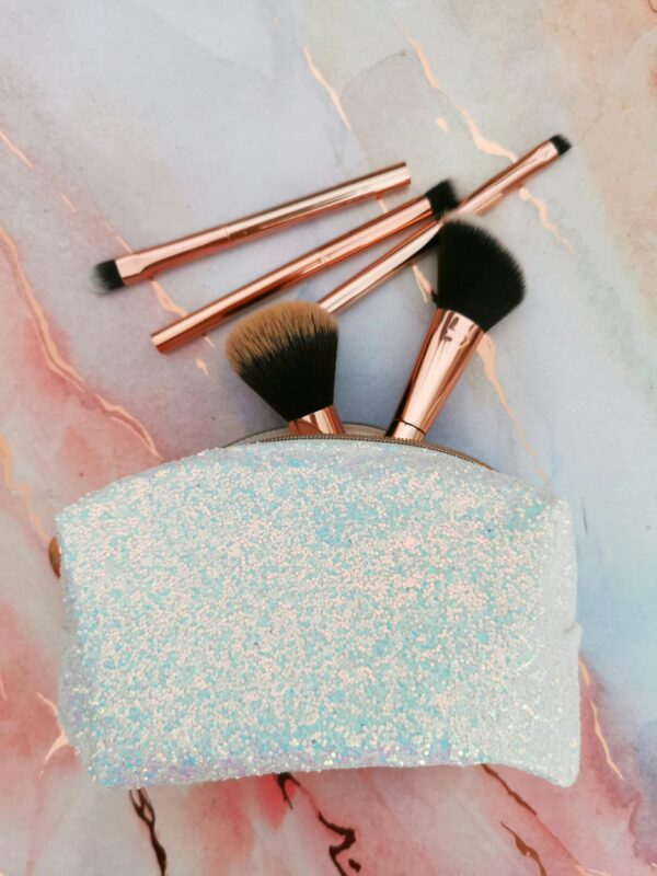 Shimmering makeup pouch with brushes on marble background. Perfect for beauty enthusiasts.