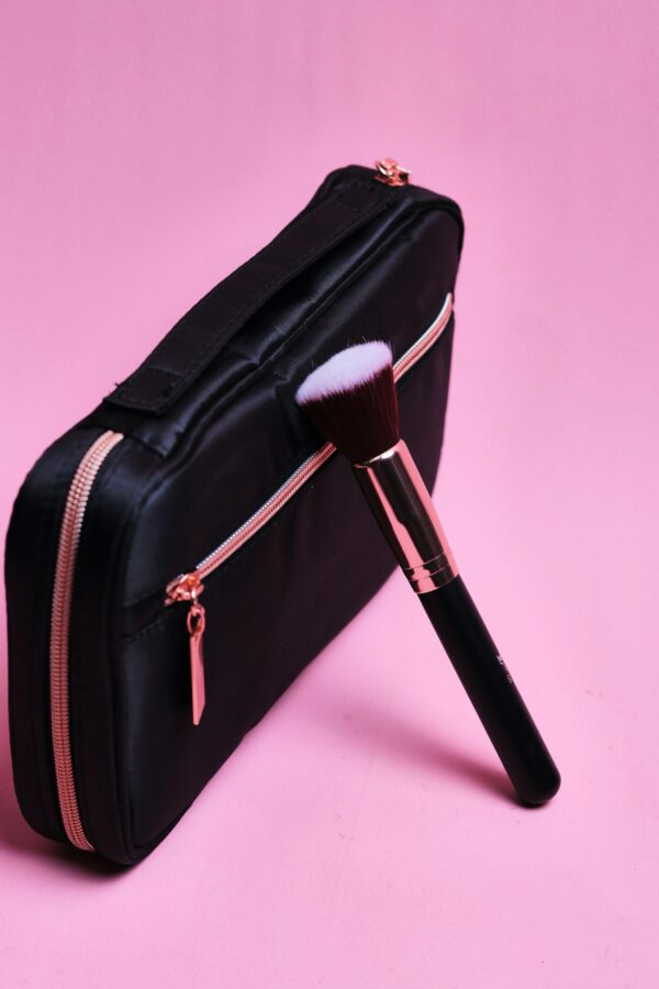 Stylish black makeup bag paired with a brush against a pink background, perfect for glamour and fashion themes.